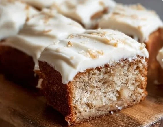 Moist banana cake with cream cheese frosting on a white plate