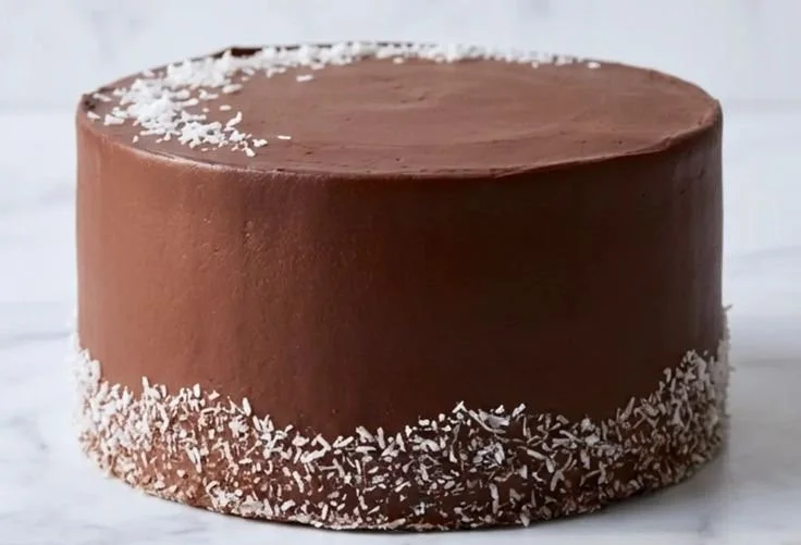 Deliciously moist Chocolate Coconut Cake topped with coconut flakes and chocolate frosting.