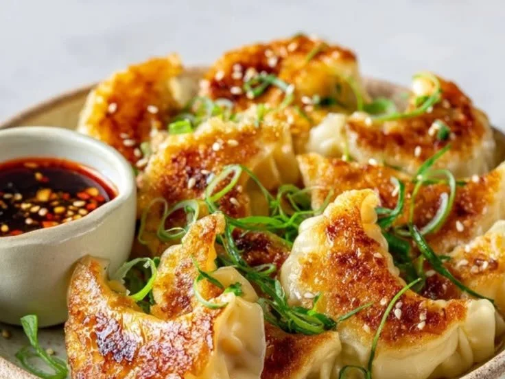Crispy pan-fried dumplings served on a plate with dipping sauce