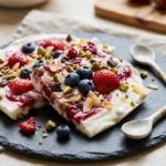 Colorful frozen yogurt bark topped with fruits and nuts on a marble surface.